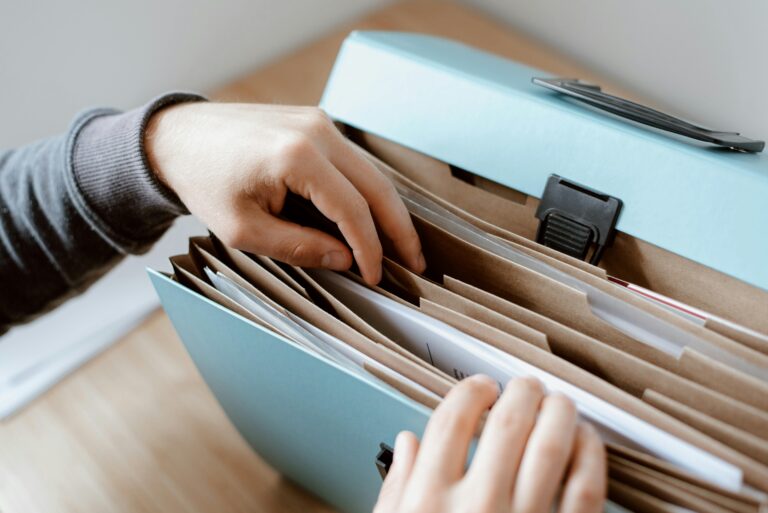 This image shows a person carefully sorting through a file organizer filled with employee documents. It represents the importance of maintaining accurate and up-to-date employee records—crucial for HR compliance, performance tracking, and administrative efficiency. Proper documentation ensures seamless access to essential employee information when needed.